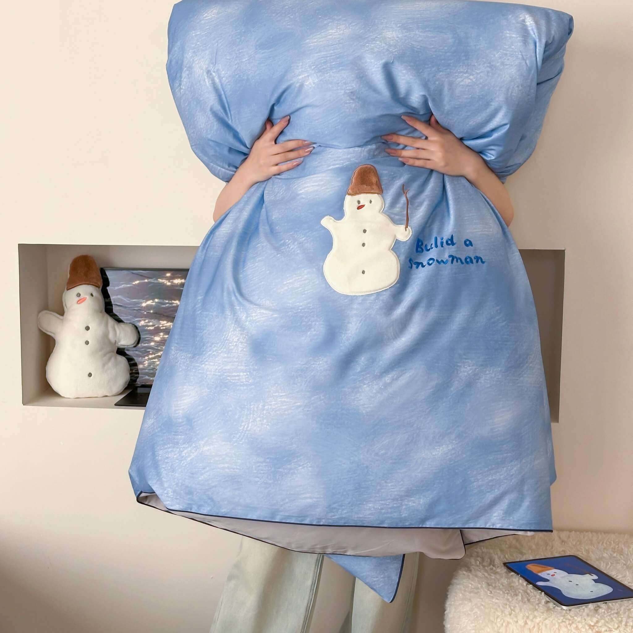 a person holding a blue quilt with a snowman design and standing in front of a wall