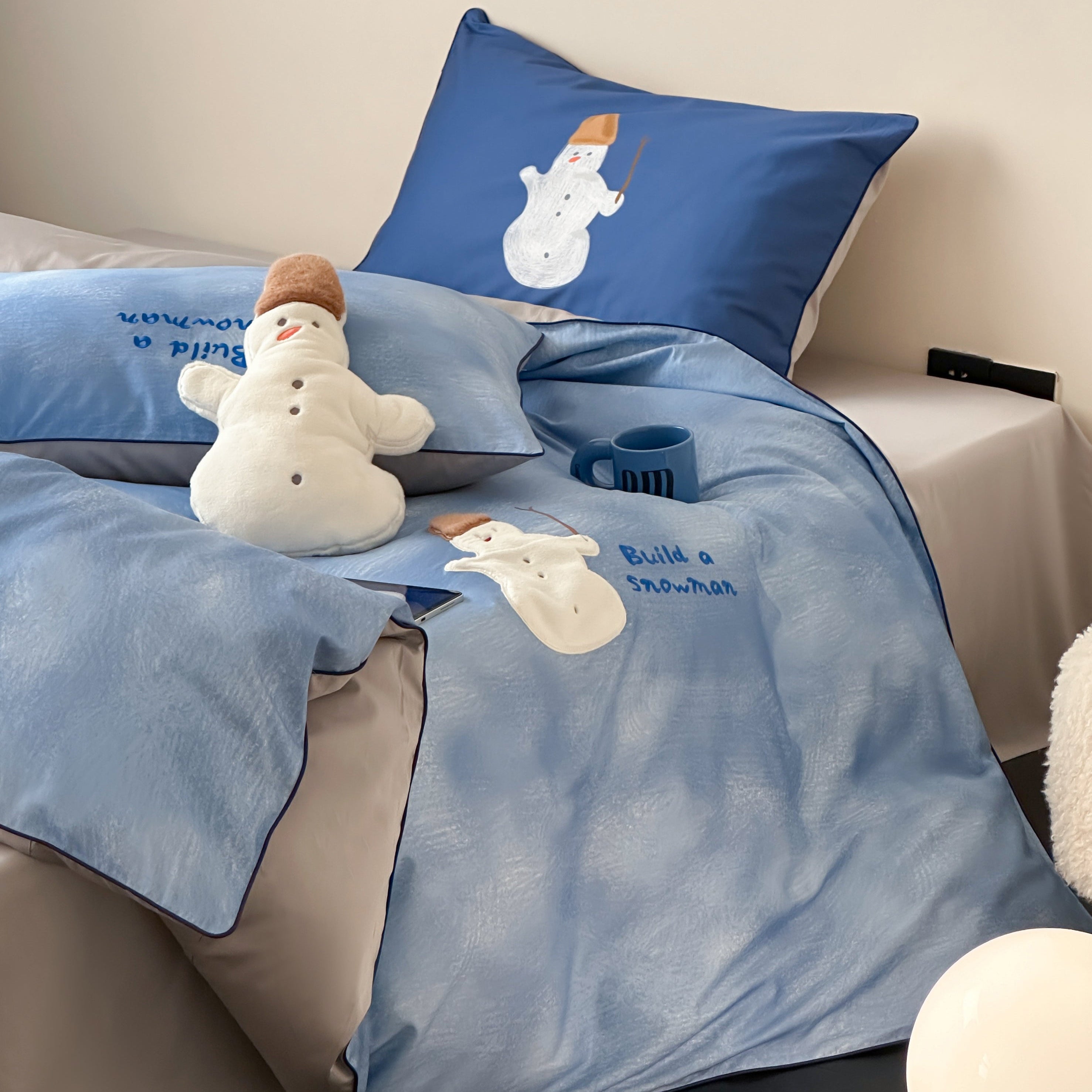 Blue cotton bedding set with embroided snowman and blue sky design on a bed in a room.
