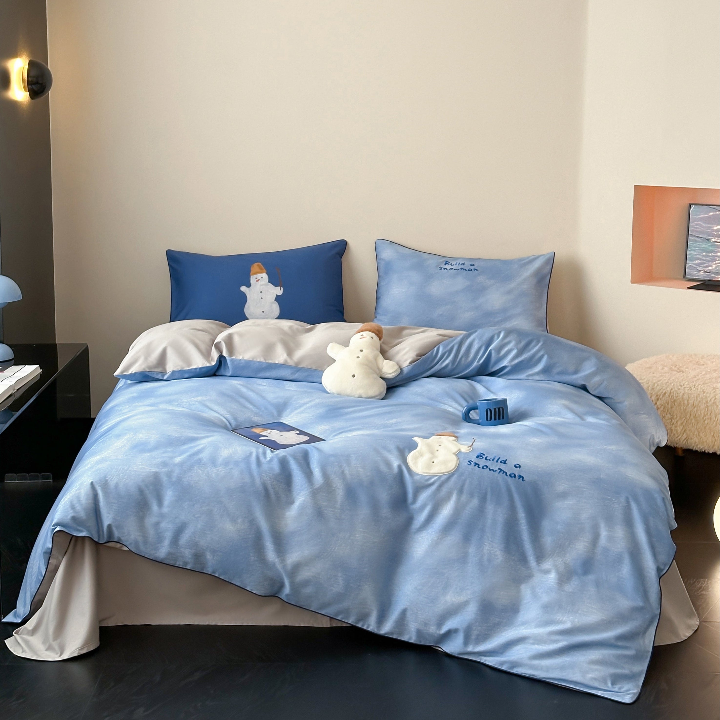Blue cotton bedding set with embroided snowman and blue sky design on a bed in a room.