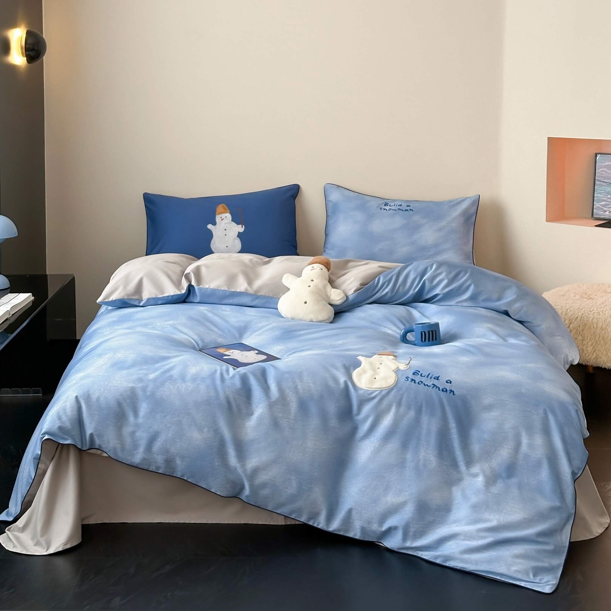 Blue cotton bedding set with embroided snowman and blue sky design on a bed in a room.