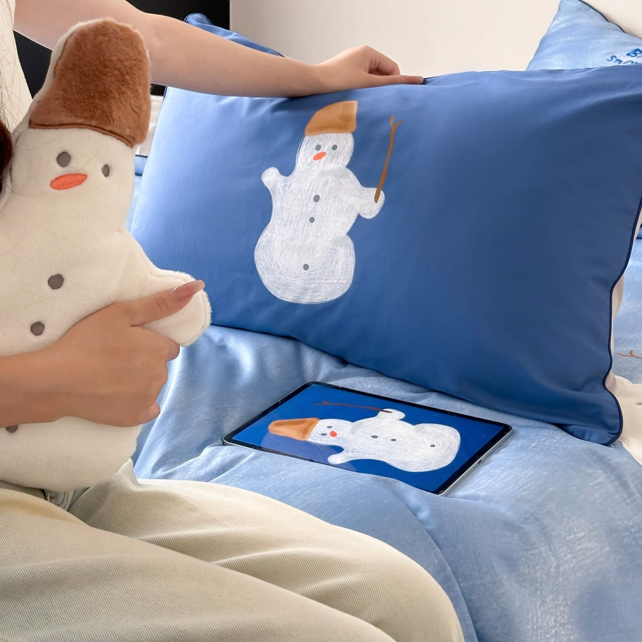 Person holding a plush snowman cushion with a matching pillow featuring a snowman design.