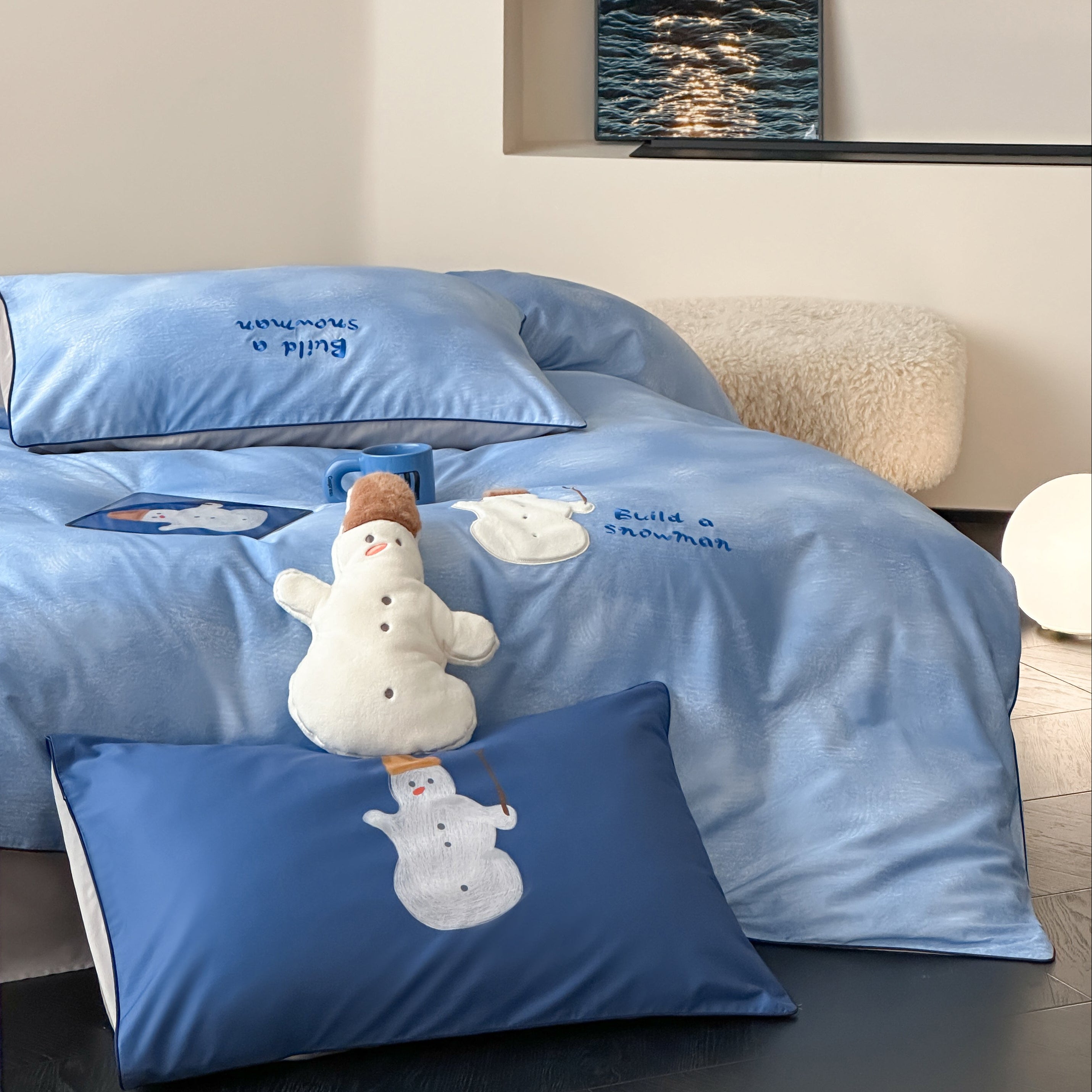 Blue cotton bedding set with embroided snowman and blue sky design on a bed in a room.